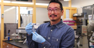 ESF professor Chris Nomura holds test tube with rubber gloves on in science lab.