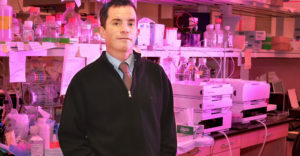 Upstate Medical University professor Kerr stands in front of medical lab shelves.