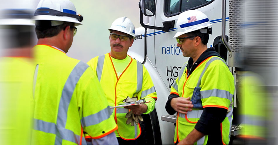3 National Grid gas workers talk in front of a company utility truck. 