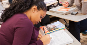 An african-american EOP student writes notes at her desk in a classroom at Buffalo State.