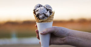 Outstretched hand holds ice cream in waffle cone.
