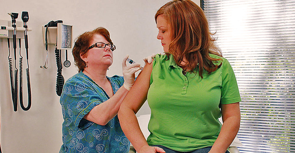In doctor's office, a female nurse gives a female patient a vaccine shot in her right arm. 
