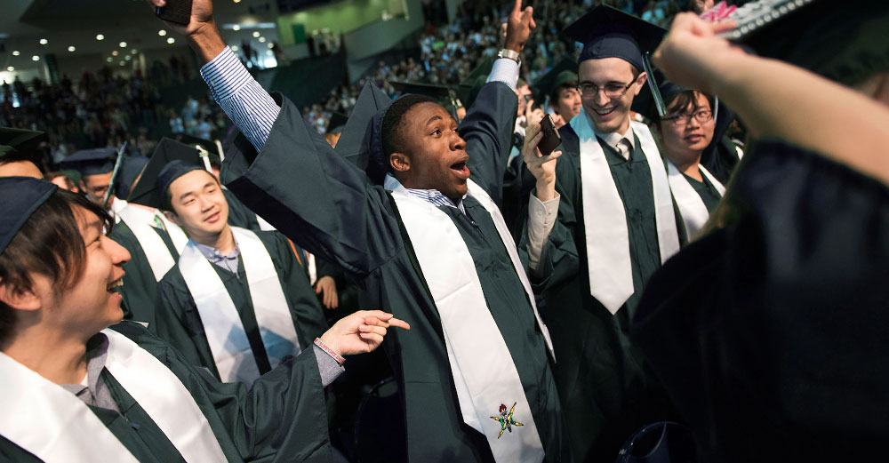 Binghamton University graduate pumps his arms in the air to celebrate in the crowd at commencement.