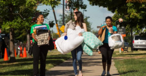 Female students at Buffalo State carry bags and boxes during move-in day.