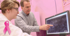 SUNY Poly professor Dr James Castracane points at computer screen with cancer cell diagaram as a female student looks on
