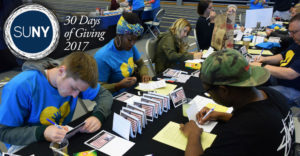 Onondaga Community College students sign thank you cards for veterans sitting at a larget table.