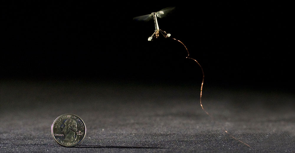 A tiny robotic drone flies right abobe a quarter to show it's size comparison.
