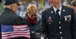 A military service member student at Buffalo State shakes hands with a veteran senior citizen soldier.