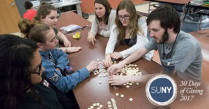 Binghamton University students play with scrabble pieces at a table.