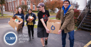 SUNY Geneseo students carry boxes of food and non-perishable items up a driveway.