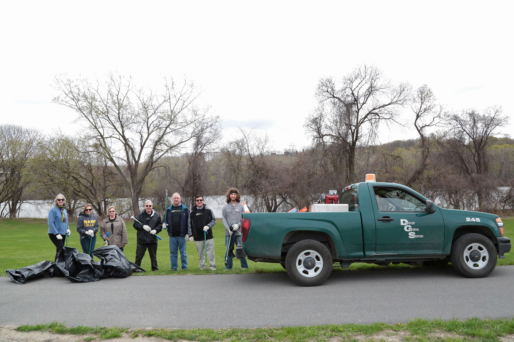 SUNY Poly staff with NYS Dept of General Services truck in front of them as they clean up outdoor park space.
