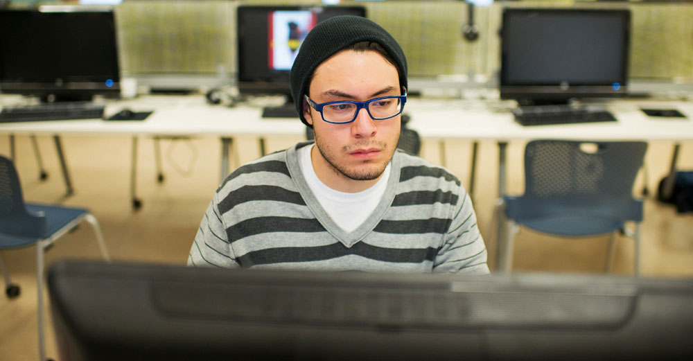 Male student at SUNY Plattsburgh sits at computer station in computer study lab.