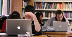 Student looks down and stressed outwith his hand holding his head up in the library.