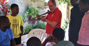 Bill Cole holds up a woodwind horn as he teaches locals in Haiti about it.