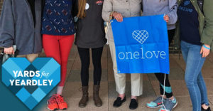 A group of women stand holding a OneLove banner before walking iin a Yards For Yeardley event.
