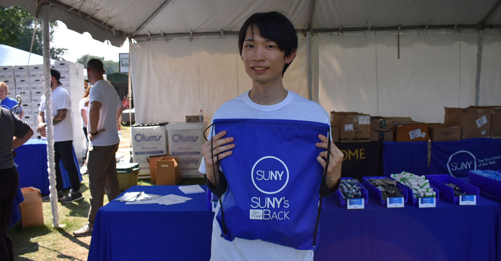 Daiki Yoshiok stands in the SUNY's Got Your Back tent holding a bag up.