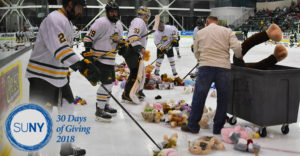 SUNY Oswego hockey players help clean teddy bears off the ice during a game.