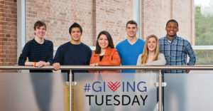 Students line up behind a short railing with Giving Tuesday laying in front of it.