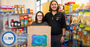 A male and female SUNY Broome student stand inside a food pantry with loaded shelves of food stuff.