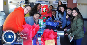 SUNY Orange students package blankets and jackets into boxes covered in christmas gift wrapping for donation.