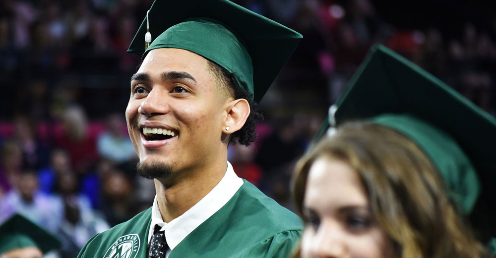 Smiling male student stands during Mohawk-Valley Community College commencement.
