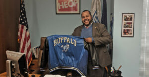 NYS Assemblyman Victor Pichardo in his office holding up his old UBuffalo jacket.