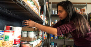 Female student reaches for food items in New Paltz campus food pantry.