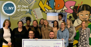 Monroe Community College students and staff pose with a giant check being donated to their local Boys and Girls Club.