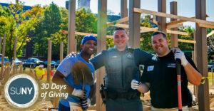New Paltz student and staff member with a university police officer at a build site for a playground.