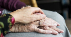 A senior citizen's hand is on its lap being held under a younger person's hand.