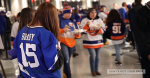 NY Islanders fans walk the concourse at a game with someone in a SUNY's Got Your Back jersey in the foreground.
