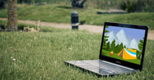 A laptop placed on the grass in a park with a screen showing a camping tent.