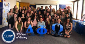 Members of the SUNY New Paltz student-led chapter of Alpha Phi Omega pose in front of the greek letters.