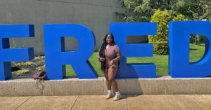 Tanique McLune in front of stonr FRED sign at SUNY Fredonia.