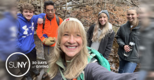 FMCC professor Paula Brown-Weinstock takes a selfie with students behind her in the woods while on a hike.