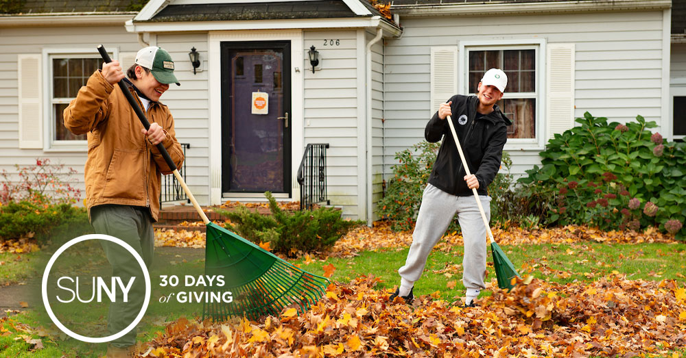 2 male students rake leaves on a house lawn.