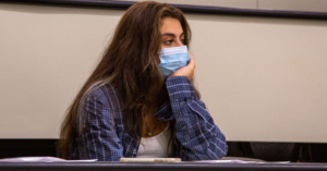 Female student wearing a face mask looking tired in class lecture hall.