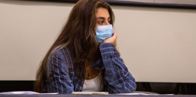 Female student wearing a face mask looking tired in class lecture hall.