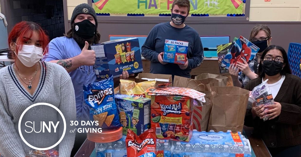Students wearing face masks stand behind a large table full of food items being packed for donations.