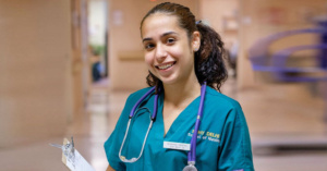 Female nursing student in uniform with stethoscope around her neck smiles.