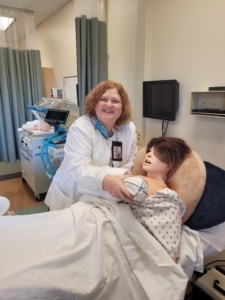 Mary Lee Berg, a nursing faculty member at SUNY Onondaga Community College, holding an animatronic baby on an animatronic patient in the training lab of OCC.