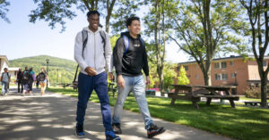 2 male college students walk outside along tree lined path.