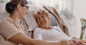Young female social worker helps old lady in a bed.