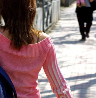 Woman walks along city street with backback on one shoulder.