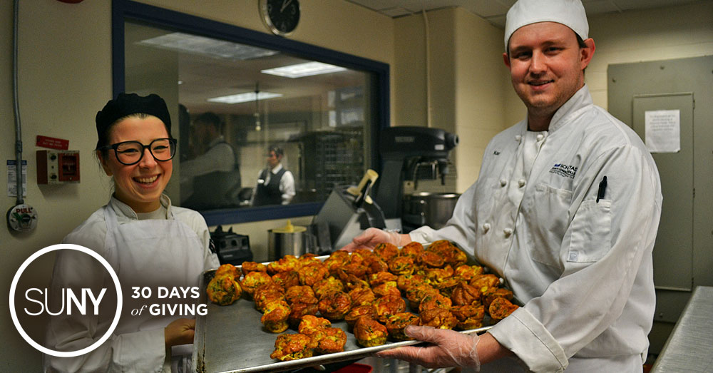 Culinary students at Schenectady County Community College hold a large tray of cooked chicken in the schools kitchen classroom.