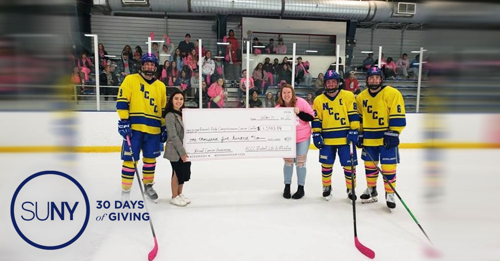 Members of the Niagara County Community College hockey team on the ice during intermission with staff holding a giant check for a donation to Roswell Park Cancer Center.
