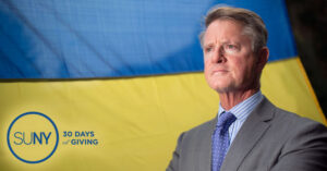 Dr Gregory Gardner with a Ukranian flag behind him.