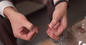 Hands stretch out a printed copper circuit.