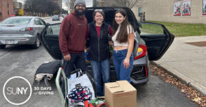Two students and a staff member at SUNY Plattsburgh stand behind boxes of food stuff to be loaded into a car for a food drive donation.