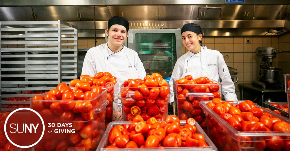 Two culinary arts students in stand behind tubs of fresh tomatoes in the SUNY Delhi teaching kitchen.